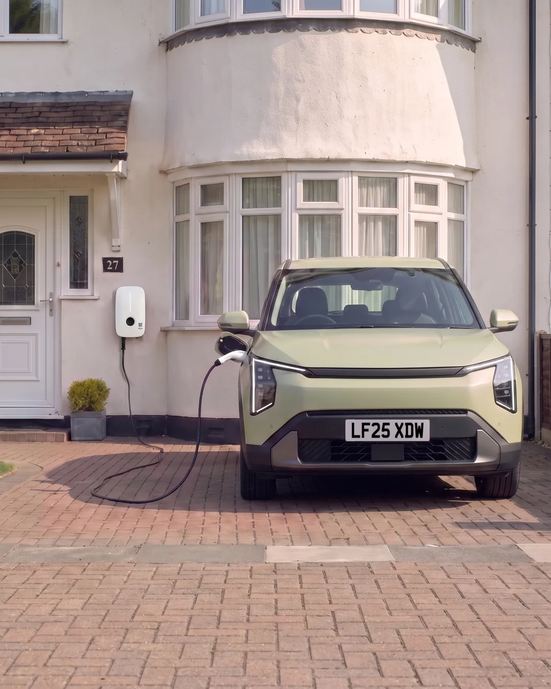 Maya's green car on Martin's drive, plugged into his charger.