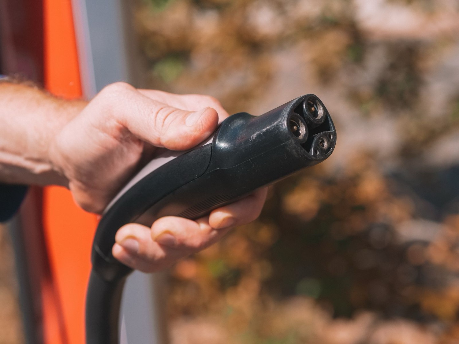A hand holding a Type 2 EV charging connector outdoors
